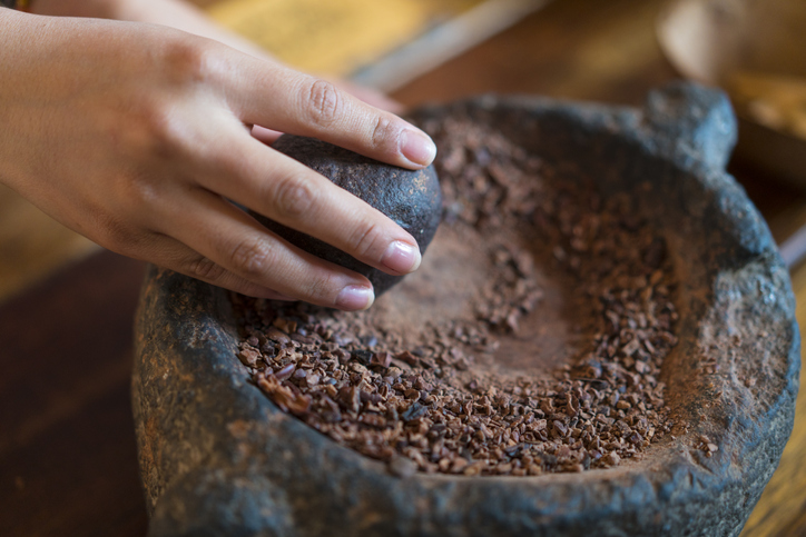 A woman’s hand with a stone grinder grinds cocoa and prepares cacao for a chocolate drink, near Otavalo, North Ecuador.